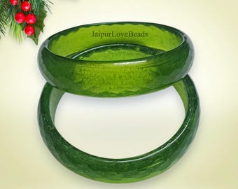 May include: Two green glass bangles stacked on top of each other. The bangles are smooth and shiny with a slight textured pattern. JaipurLoveBeads is written on the top bangle.