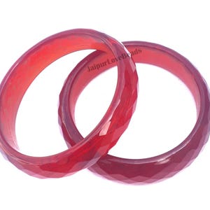 Peut inclure: Deux bracelets en pierre rouge, l'un avec une finition lisse et l'autre avec une finition facetée. Les bracelets sont empilés l'un sur l'autre.