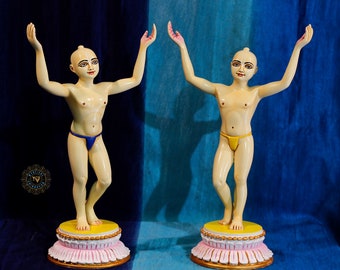 May include: Two small, white, painted figurines of people with their arms raised. The figurines are standing on yellow and pink bases. The figurines are wearing yellow and blue cloth.
