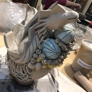 May include: A ceramic sculpture of a dragon with blue and white patterned spheres and yellow swirls. The dragon is in a curled position with its head raised.