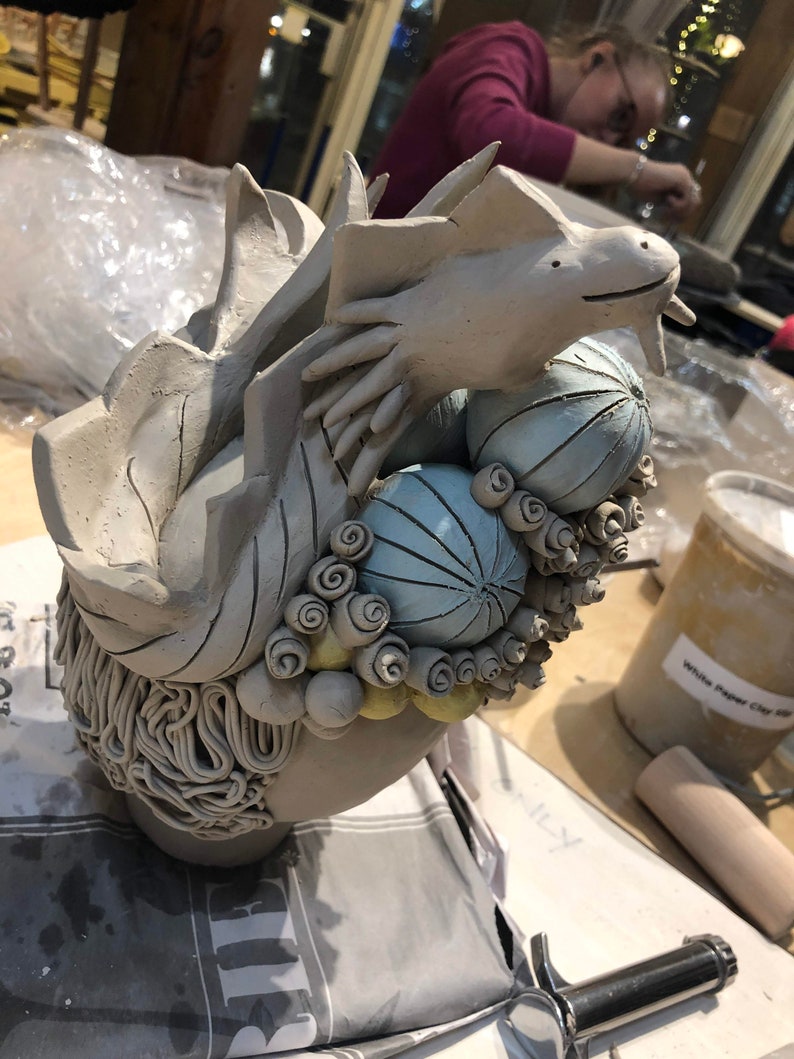 May include: A ceramic sculpture of a dragon with blue and white patterned spheres and yellow swirls. The dragon is in a curled position with its head raised.
