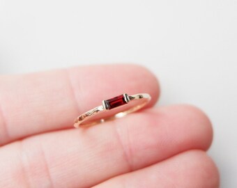 May include: A gold ring with a single, rectangular, red gemstone.