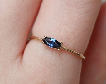 May include: A delicate gold ring with a marquise-shaped blue sapphire gemstone.