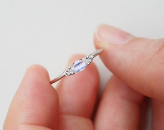 May include: A silver ring with a light blue oval gemstone and two smaller clear gemstones on either side.