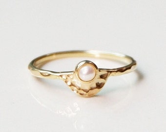 May include: A gold ring with a textured band and a small pearl in the center.
