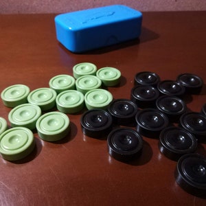May include: A set of green and black carrom game pieces. The pieces are arranged in a pattern on a wooden surface. There is a blue box in the background.