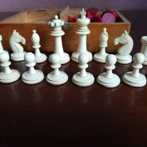 May include: A set of white chess pieces made of ivory. The pieces include pawns, knights, bishops, rooks, a queen, and a king. The pieces are arranged on a wooden surface.