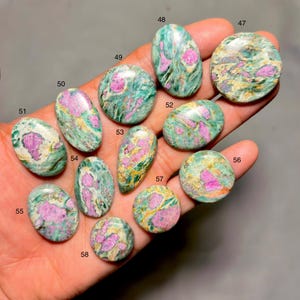 Puede incluir: Una colección de piedras preciosas pulidas en varias formas, incluyendo ovaladas y redondas. Las piedras presentan una mezcla de tonos verdes, rosas y amarillos, con un patrón veteado o arremolinado. Las piedras preciosas se muestran en una mano.