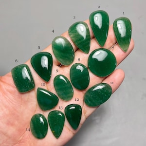 May include: A selection of fourteen polished green gemstones in diverse shapes, such as teardrop, oval, and round. The gemstones are held in a hand, displaying their vibrant colour and smooth surfaces. The sizes vary, with some appearing larger than others.