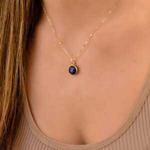 May include: A gold chain necklace with a small, round, dark blue gemstone pendant.