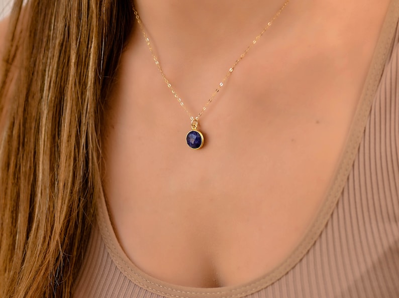 May include: A gold chain necklace with a small, round, dark blue gemstone pendant.