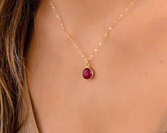 May include: A gold chain necklace with a round, red gemstone pendant.