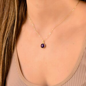 May include: A gold chain necklace with a small, round, purple gemstone pendant.
