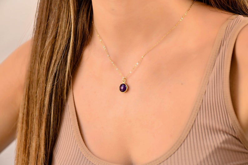 May include: A gold chain necklace with a small, round, purple gemstone pendant.