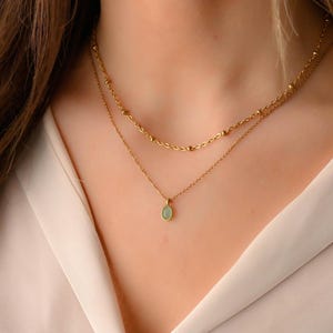 May include: A gold chain necklace with a delicate teardrop pendant featuring a light green gemstone.