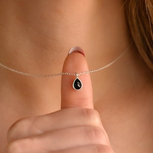 May include: A silver chain necklace with a small teardrop-shaped pendant featuring a black gemstone.