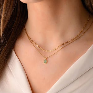 Könnte beinhalten: Eine goldene Kettenkette mit einem zarten tropfenförmigen Anhänger mit einem hellgrünen Edelstein.