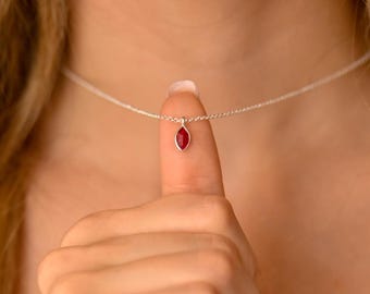 May include: A silver chain necklace with a small red gemstone pendant.