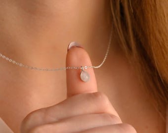 May include: A silver chain necklace with a teardrop-shaped pendant featuring a white gemstone.
