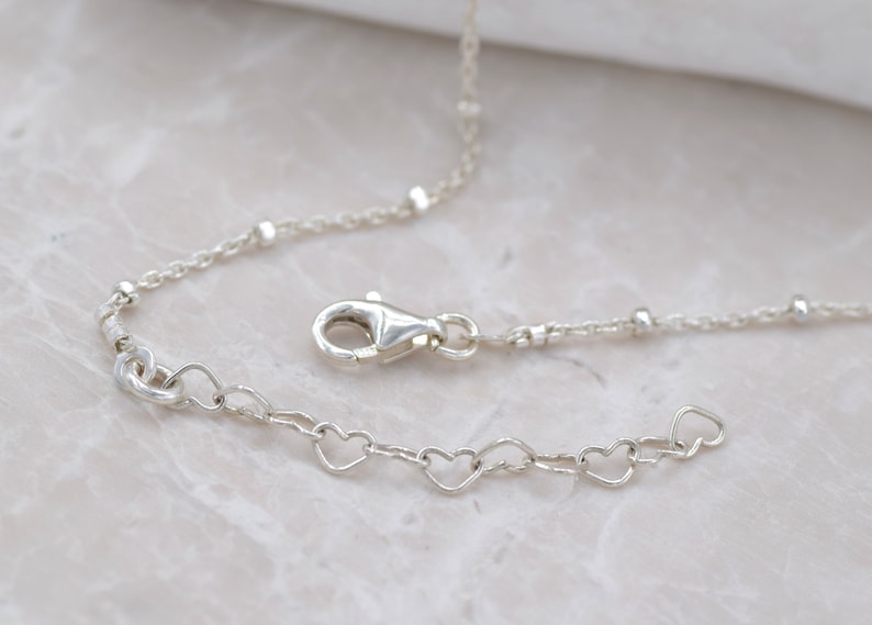 Puede incluir: Un collar de cadena de plata con una cadena en forma de coraz&oacute;n y un cierre de langosta.
