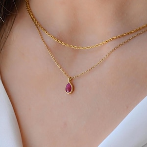 Op de afbeelding: Een gouden ketting met een traanvormige hanger met een rode edelsteen.