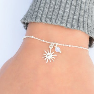 May include: A silver chain bracelet with a small silver sun charm and a white opal bead.