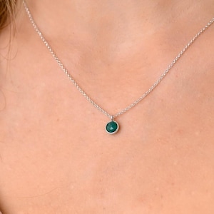 Puede incluir: Un collar de cadena de plata con un pequeño colgante redondo de piedra preciosa verde oscuro.