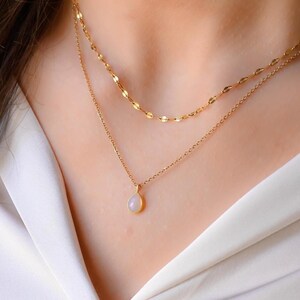 Può includere: Una collana con catena dorata con un delicato ciondolo a forma di lacrima con una pietra di opale bianca.