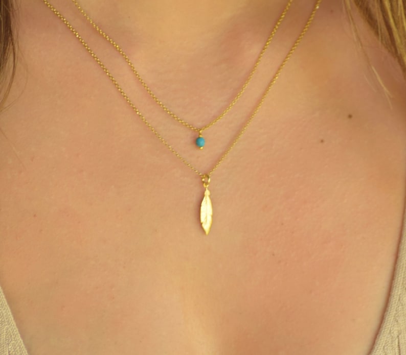 May include: A gold chain necklace with a small turquoise bead and a leaf pendant.