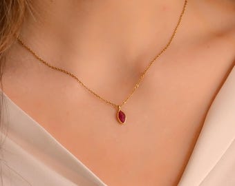 May include: A delicate gold necklace featuring a small, teardrop-shaped pendant with a vibrant red gemstone. The pendant is set in a gold bezel and hangs from a fine gold chain. The necklace is shown against a soft, neutral background.
