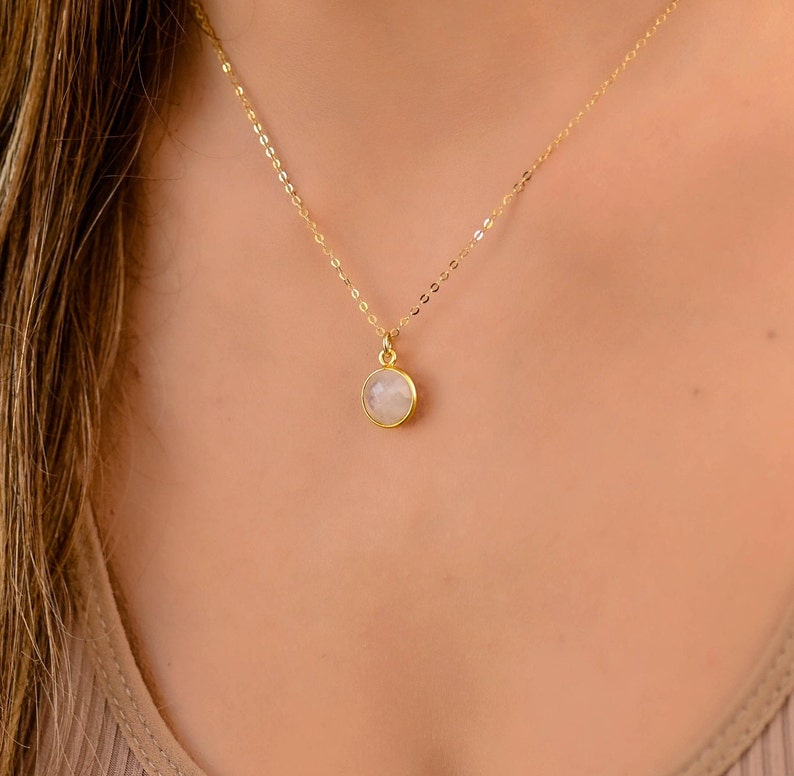 May include: A delicate gold chain necklace with a round, white gemstone pendant.