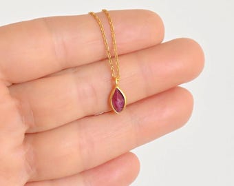 May include: A delicate gold necklace featuring a small, oval-shaped ruby pendant. The ruby is a vibrant red color, set in a gold bezel. The chain is a fine, gold link. The necklace is displayed against a neutral background.
