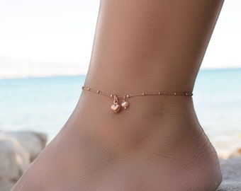 May include: A delicate rose gold anklet with a small heart charm and a pearl charm.