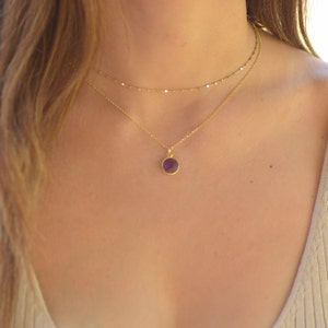 May include: A gold chain necklace with a small, round, purple gemstone pendant.
