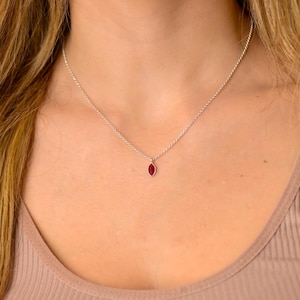 Może przedstawiać: Srebrny łańcuszek z małym, czerwonym, markizowym wisiorem z kamienia szlachetnego.