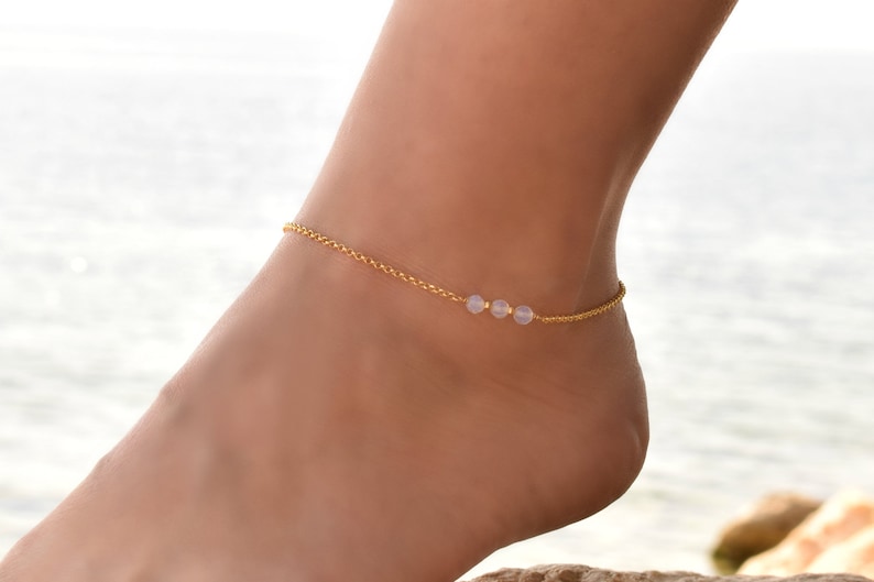 May include: A delicate gold anklet with three small, pale pink beads.