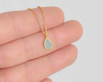 May include: A delicate gold chain necklace with a small teardrop-shaped pendant featuring a light blue gemstone.