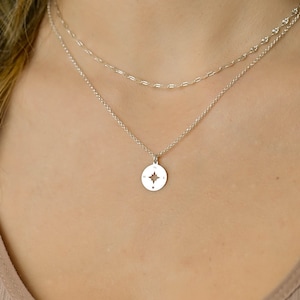 May include: A silver necklace with a compass pendant featuring a star design. The compass has the directions N, S, E, and W inscribed on it.
