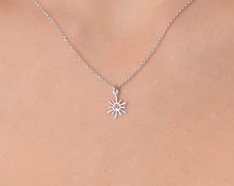 Peut inclure: Un collier en argent avec un petit pendentif en forme de soleil. Le soleil a une petite pierre précieuse rose au centre.