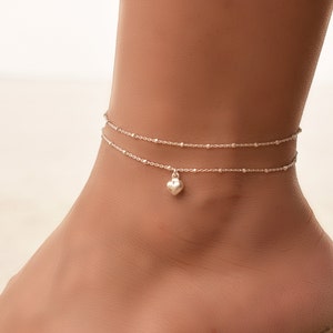 May include: Silver anklet with a delicate chain and a small heart charm.