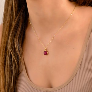 May include: A delicate gold chain necklace with a small, round, red gemstone pendant.