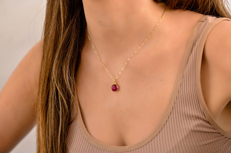 May include: A delicate gold chain necklace with a small, round, red gemstone pendant.