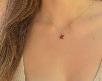 May include: A gold chain necklace with a small, round, red gemstone pendant.