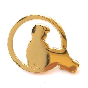 Puede incluir: Pin dorado con la silueta estilizada de una persona sentada dentro de un marco circular. La figura se muestra de espaldas al espectador. El pin tiene una superficie pulida y reflectante. El diseño es simple y elegante.