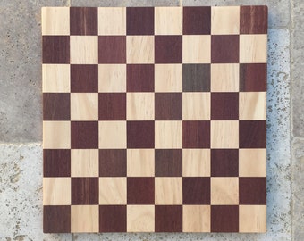 May include: A wooden checkerboard with alternating light and dark squares. The board is made of two different types of wood, one light and one dark.