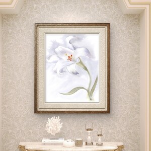 May include: A framed watercolor painting of a white flower with green leaves hangs above a gold-legged marble-topped console table. The table is adorned with decorative items. The room features built-in shelves and a light color palette.