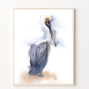 May include: Watercolor painting of a brown pelican with a long beak standing on a sandy beach. The pelican is facing to the left and has a blue and white background.
