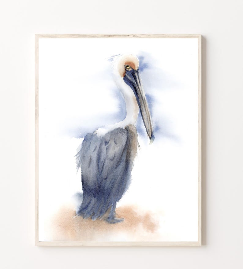 May include: Watercolor painting of a brown pelican with a long beak standing on a sandy beach. The pelican is facing to the left and has a blue and white background.