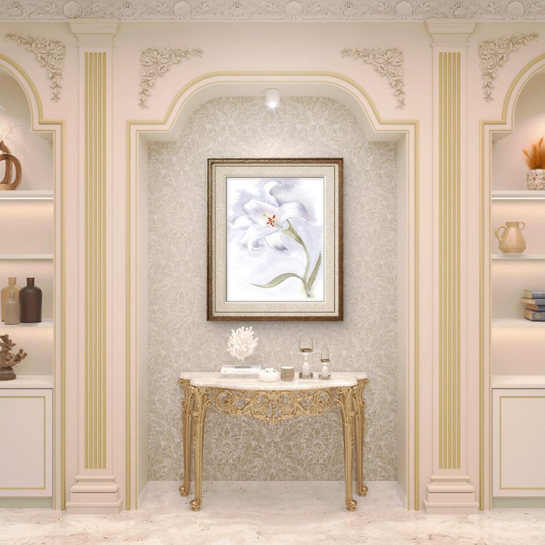May include: A framed watercolor painting of a white flower with green leaves hangs above a gold-legged marble-topped console table. The table is adorned with decorative items. The room features built-in shelves and a light color palette.