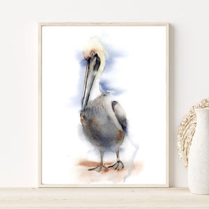 May include: Watercolor painting of a brown pelican standing on a sandy beach with a blue and white watercolor background.